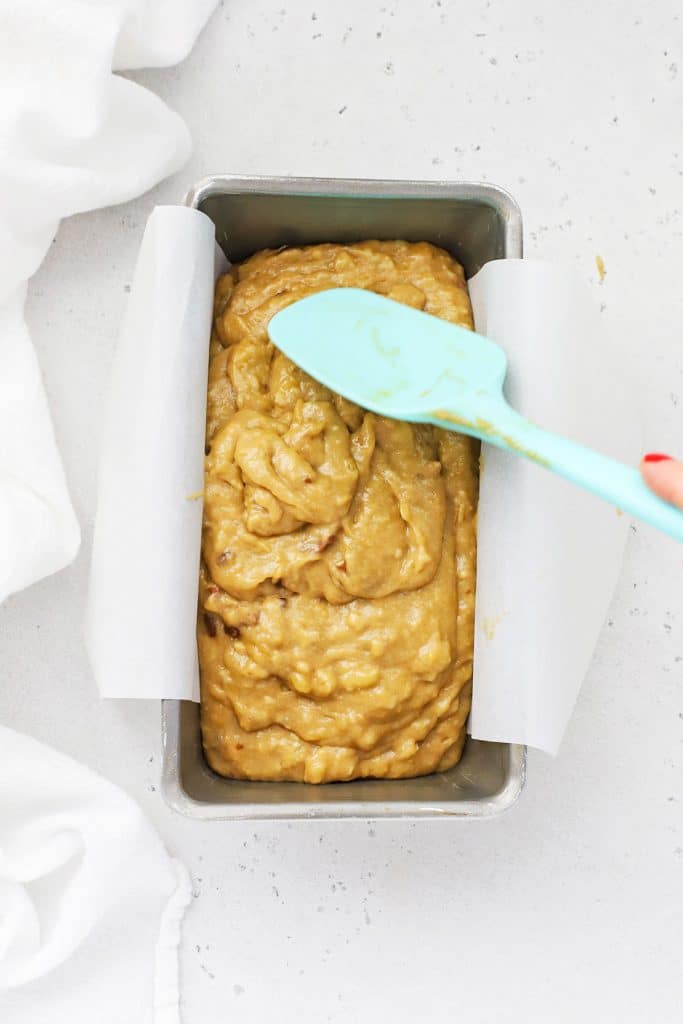 Smoothing gluten-free brown butter banana bread batter into a loaf pan lined with parchment