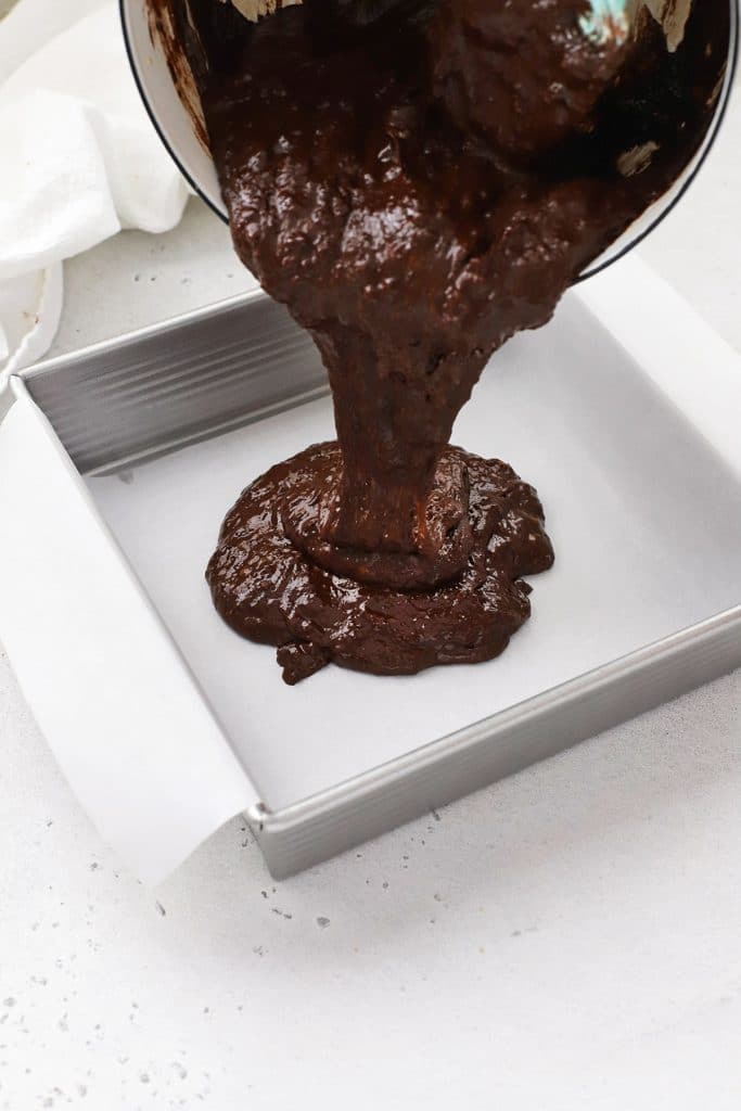 Pouring gluten-free brown butter brownie batter into a baking pan lined with parchment