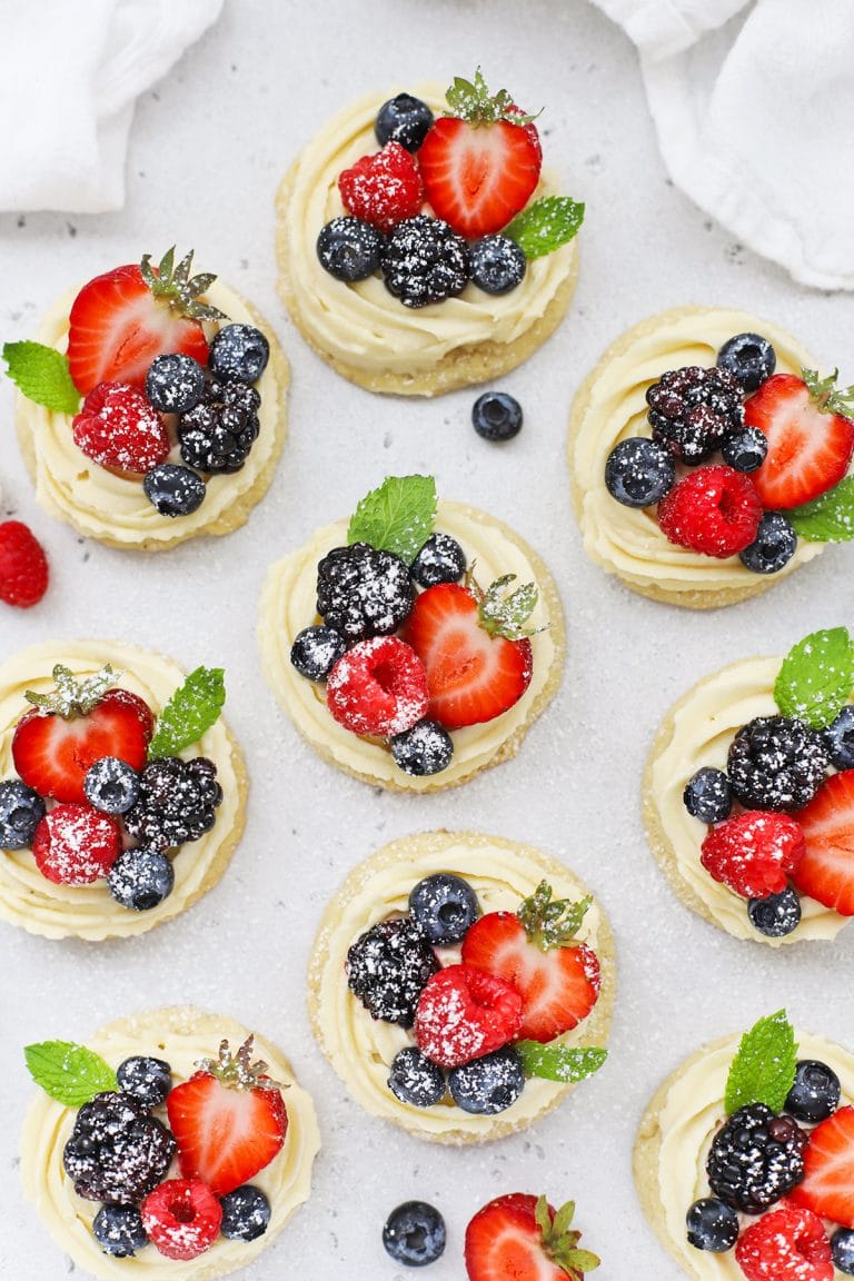 Overhead view of gluten-free fruit pizza cookies topped with cream cheese frosting berries and powdered sugar