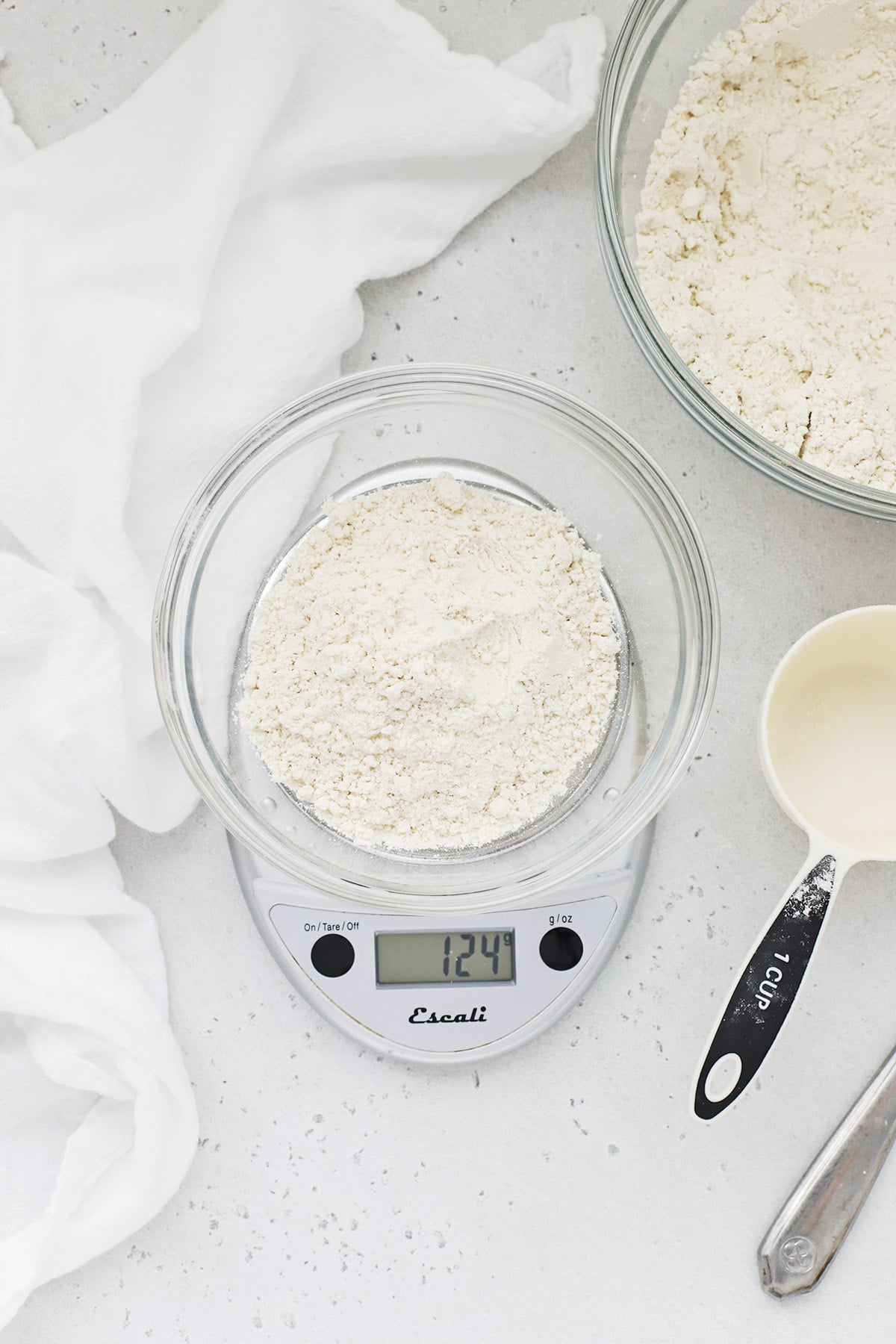 Overhead view of a bowl of flour with a measuring cup and scale for measuring properly