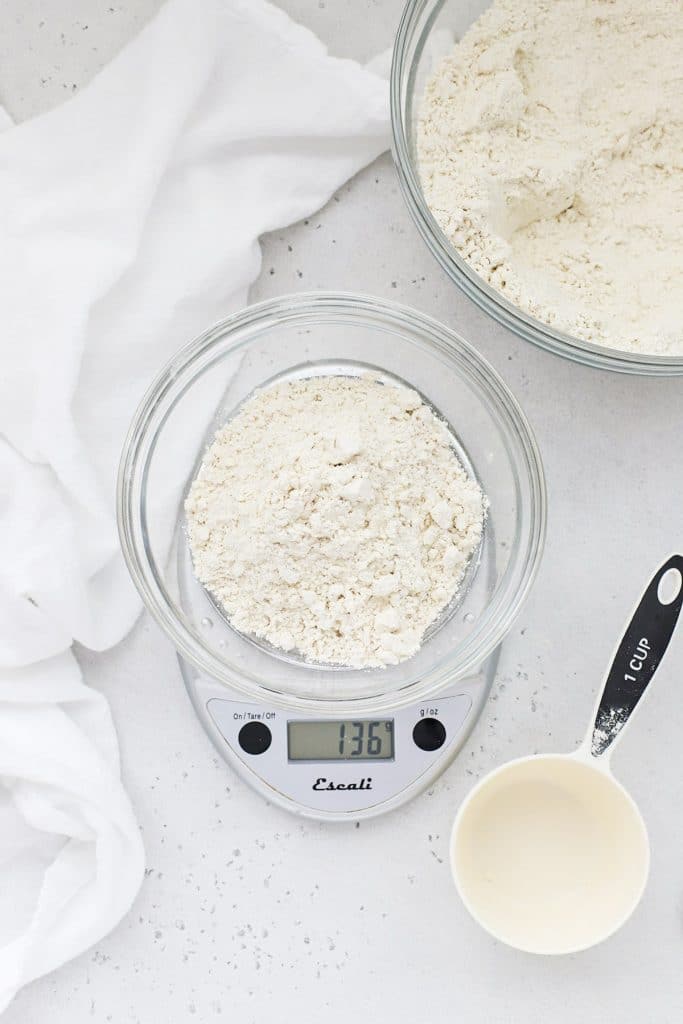 Overhead view of a bowl of flour with a measuring cup and scale for measuring properly
