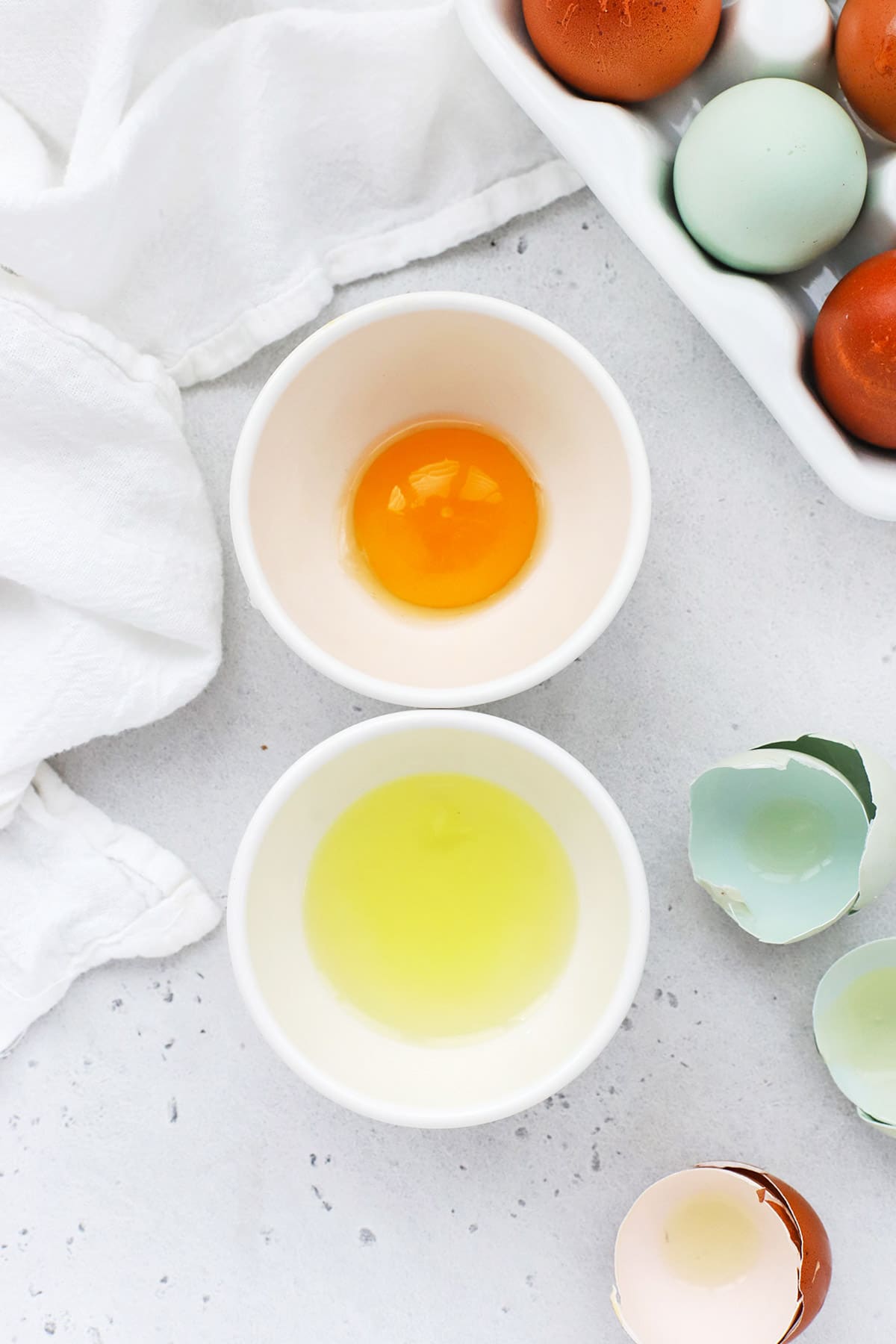 Overhead view of a separated egg, with the yolk in one bowl and the white in another bowl