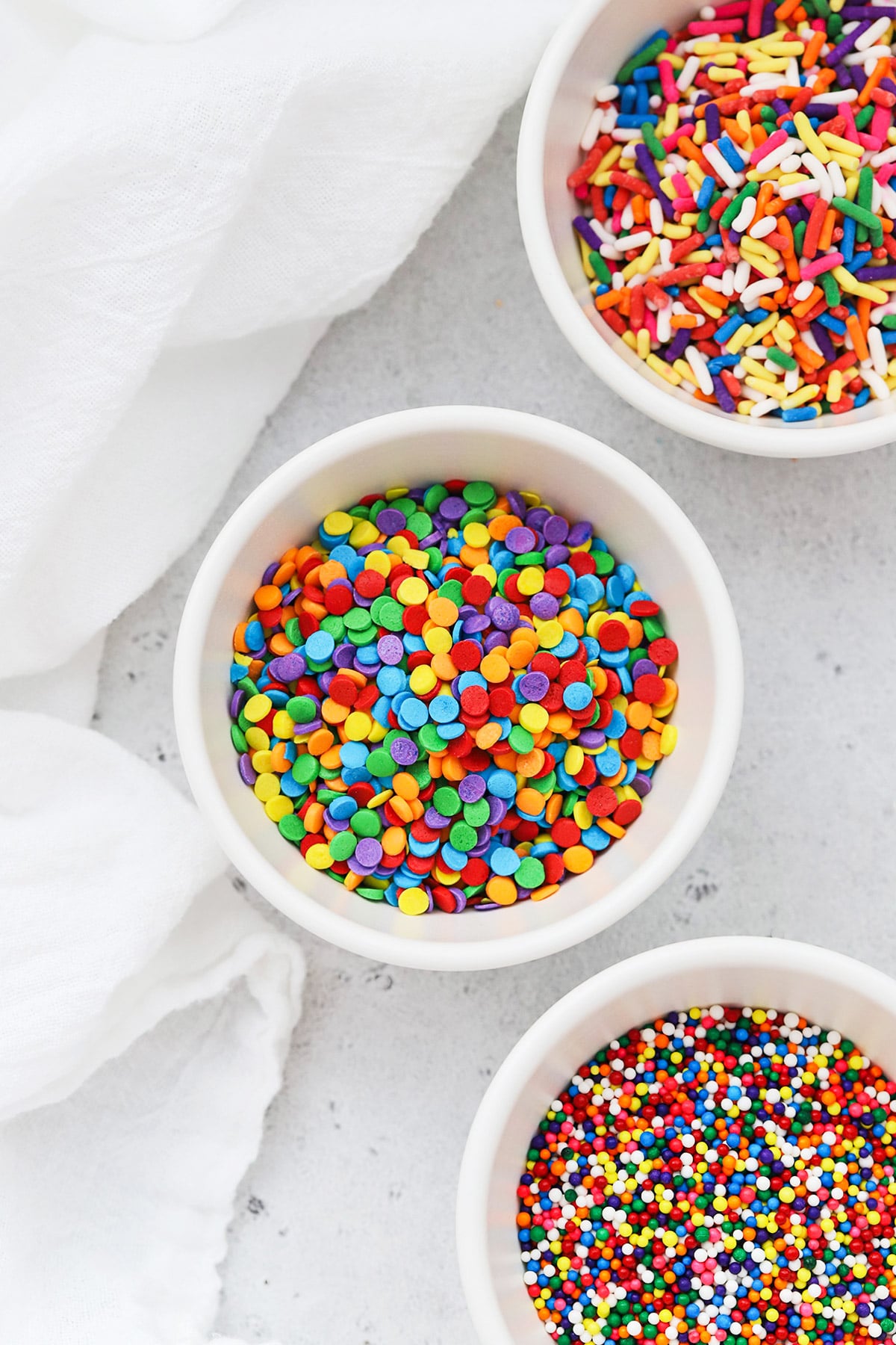 Different kinds of colorful sprinkles in white bowls