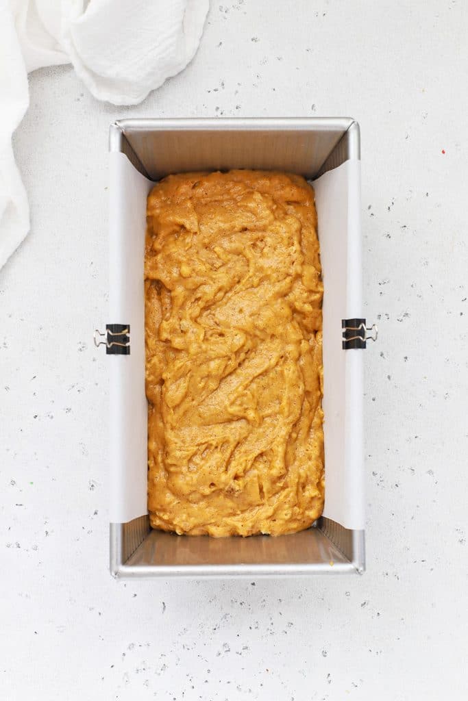 Adding gluten-free pumpkin bread batter to a loaf pan lined with parchment