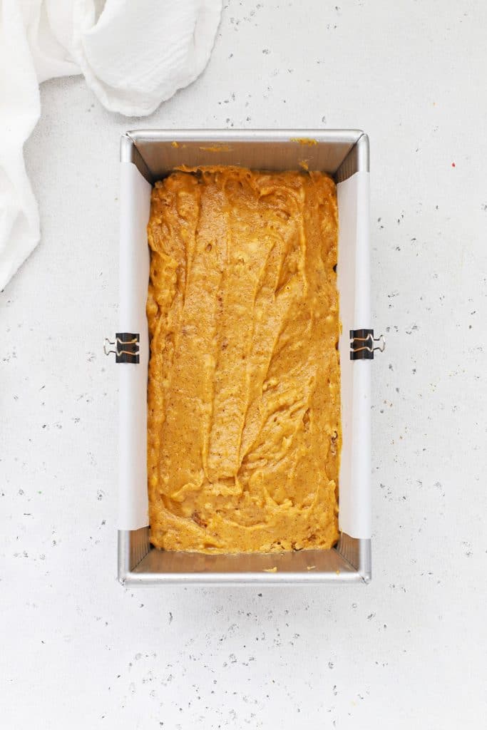 Adding a second layer of gluten-free pumpkin bread batter to a loaf pan lined with parchment