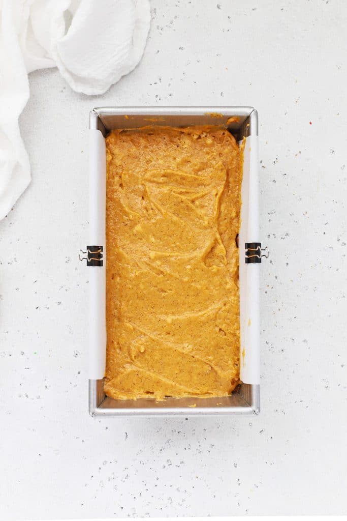 Adding a final layer of gluten-free pumpkin bread batter to a loaf pan lined with parchment