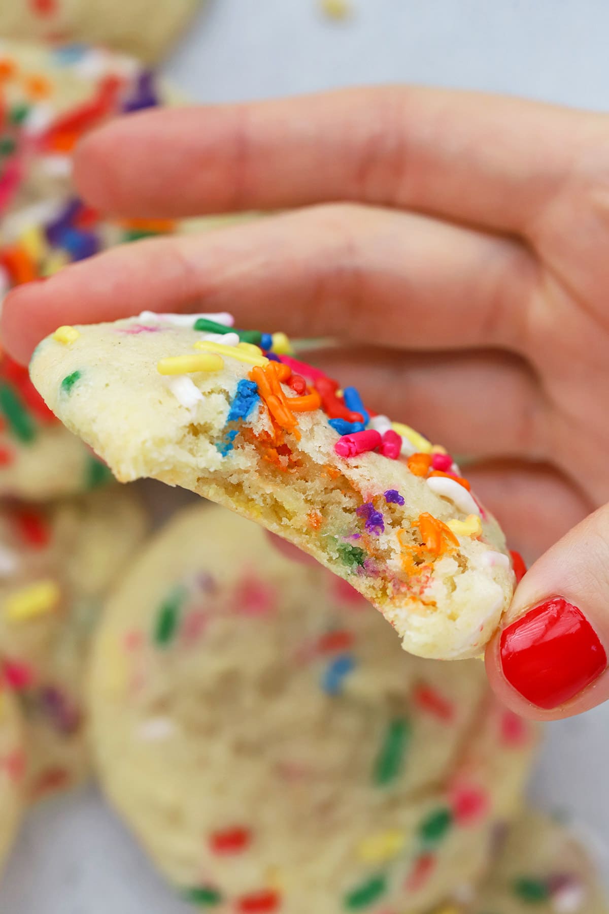 A gluten-free sprinkle sugar cookie with a bite taken out of it, revealing a soft, tender center with sprinkles