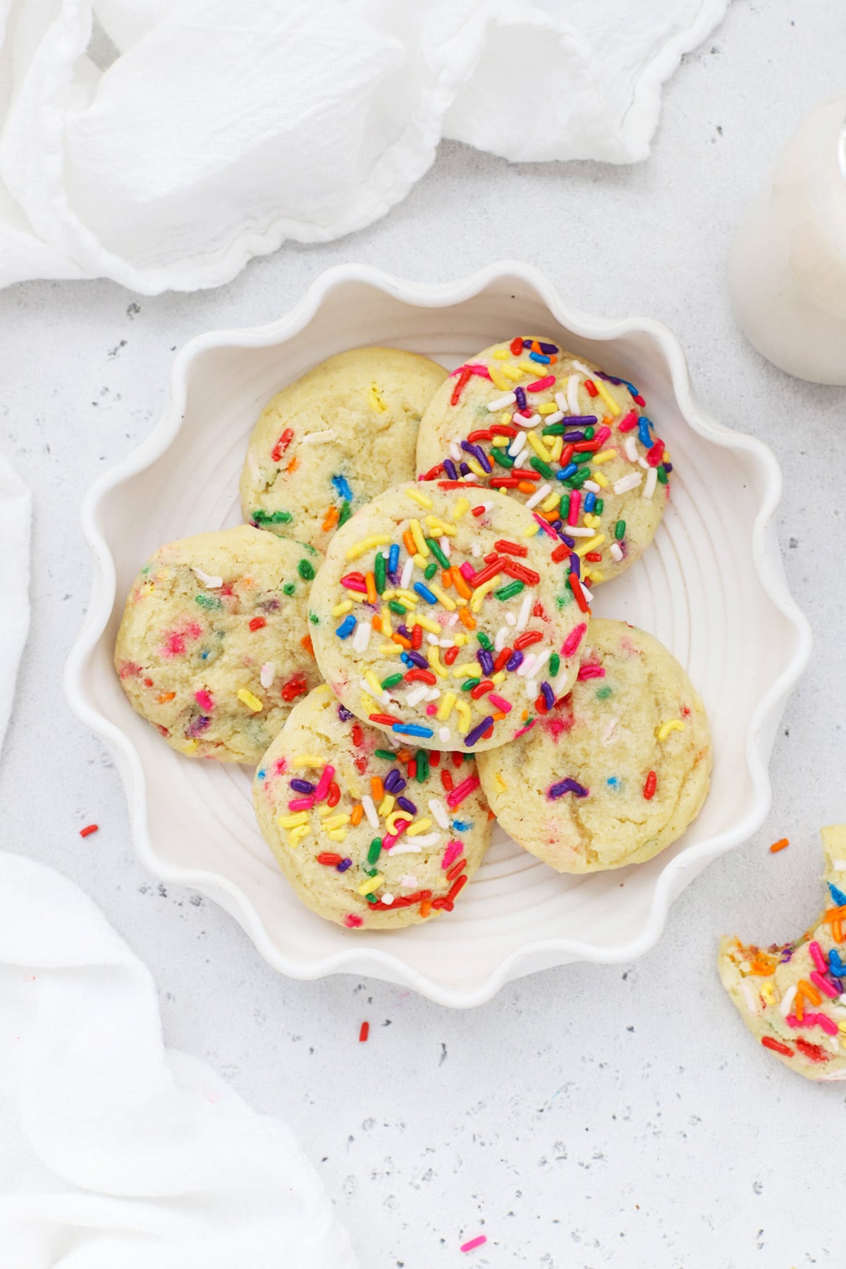 Overhead view of colorful gluten-free sprinkle sugar cookies on a white ruffled plate