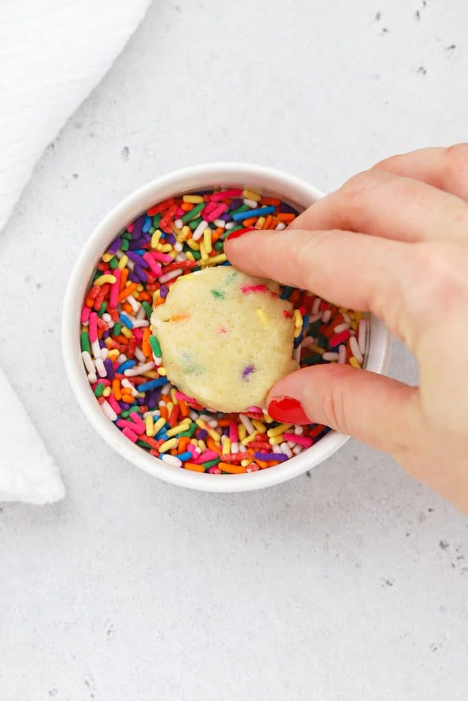 Dipping a gluten-free sugar cookie dough ball into colorful jimmies sprinkles
