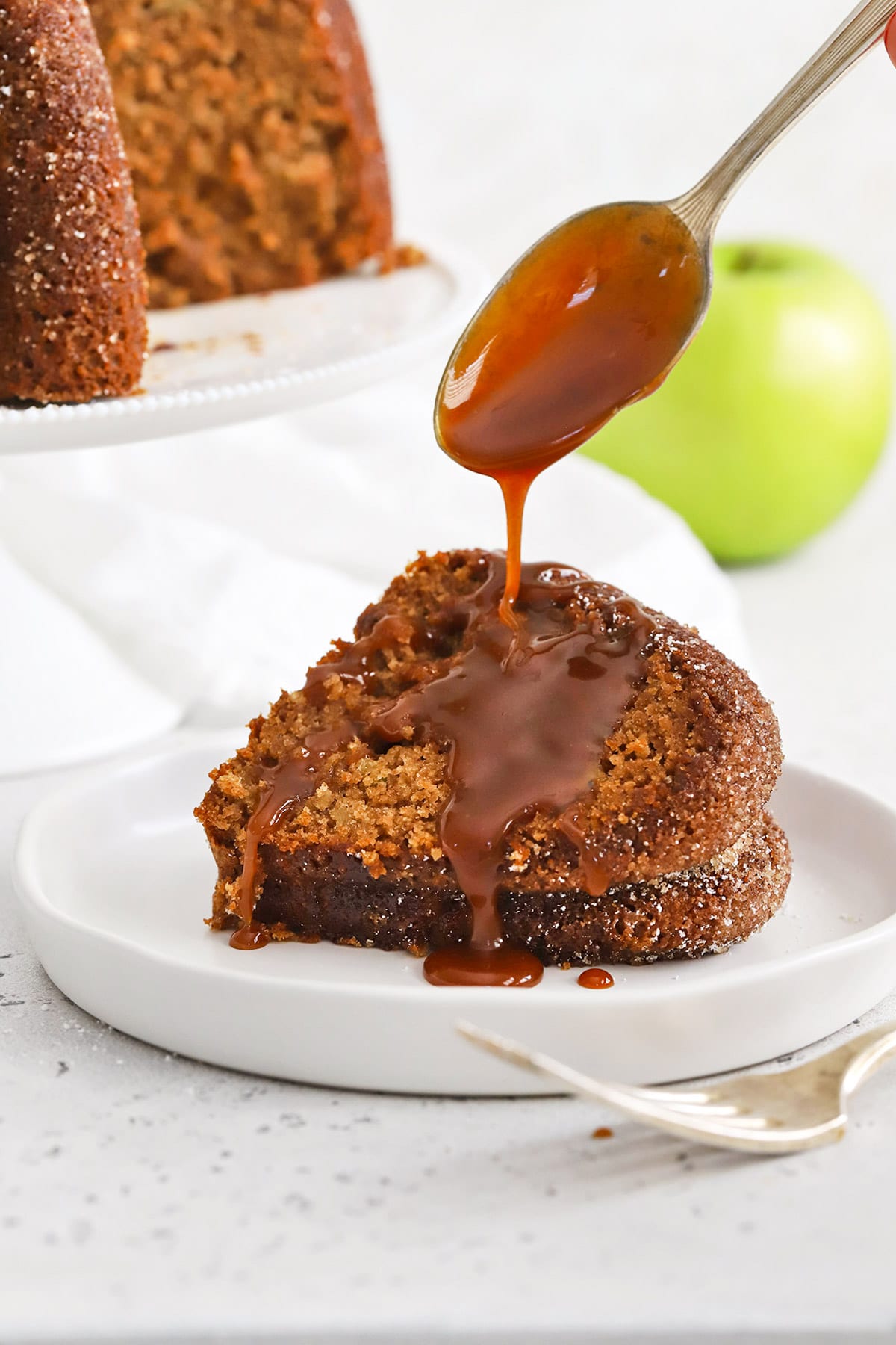 A slice of gluten-free apple spice bundt cake being drizzled with caramel sauce