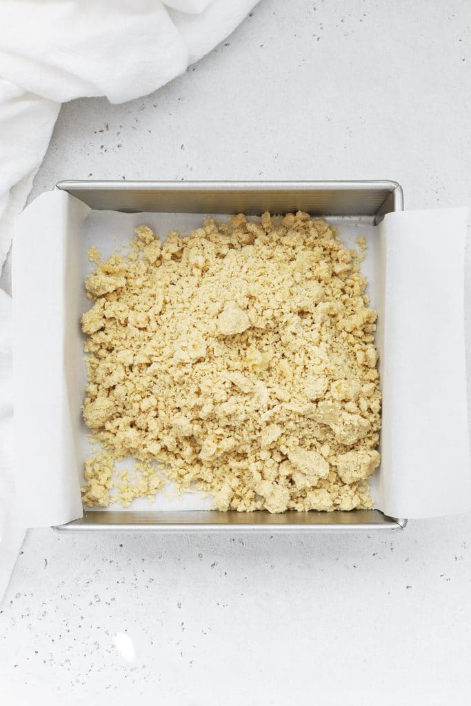 Overhead view of a crumbly gluten free brown sugar shortbread crust being transferred to a baking dish