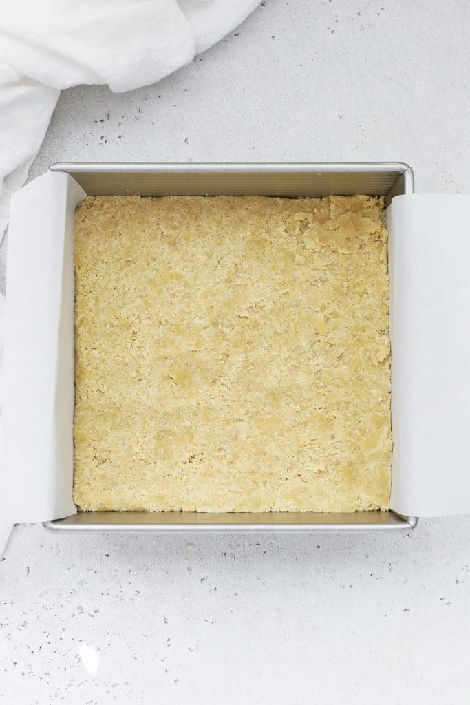 Overhead view of a crumbly gluten free brown sugar shortbread crust being patted down in a baking dish