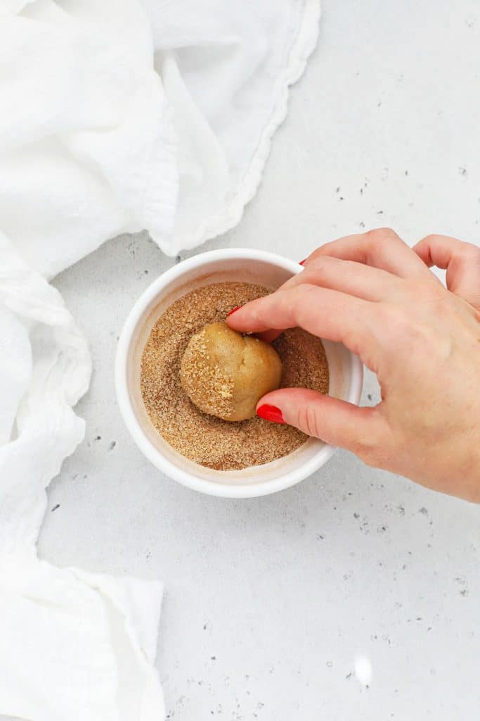 Rolling balls of gluten-free snickerdoodle cookie dough in cinnamon sugar