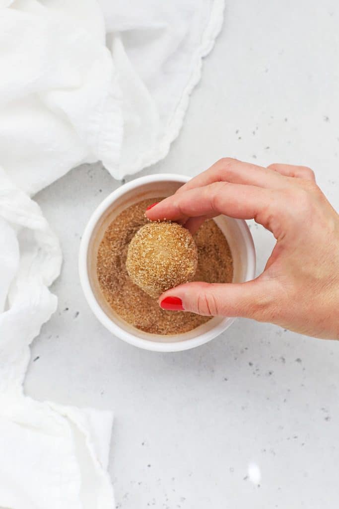 Rolling balls of gluten-free snickerdoodle cookie dough in cinnamon sugar