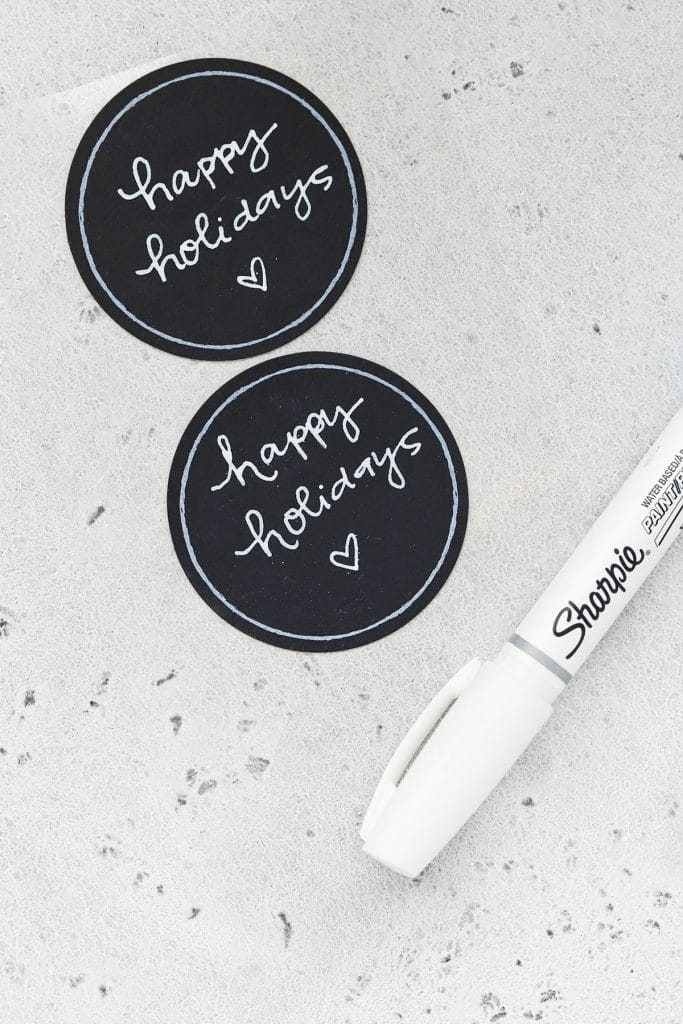 Overhead view of chalkboard circle labels with "happy holidays" written in white chalk marker