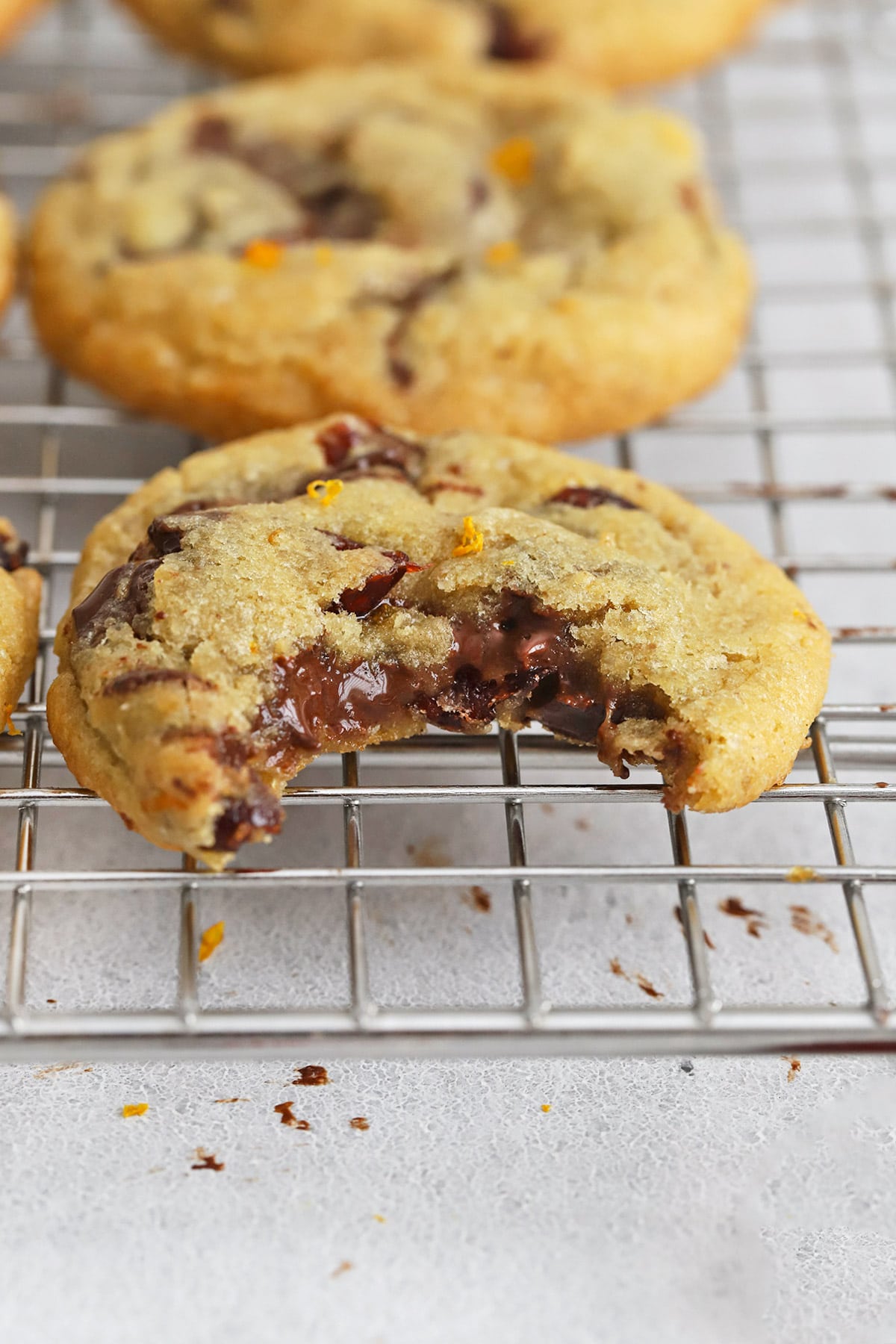 Front view of a gluten-free orange cranberry chocolate chip cookie with a bite taken out of it, revealing a gooey chocolate center