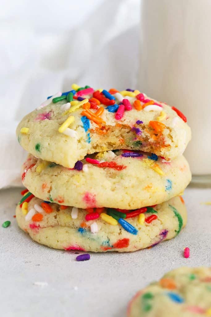 3 gluten-free sprinkle sugar cookies stacked next to a bottle of milk