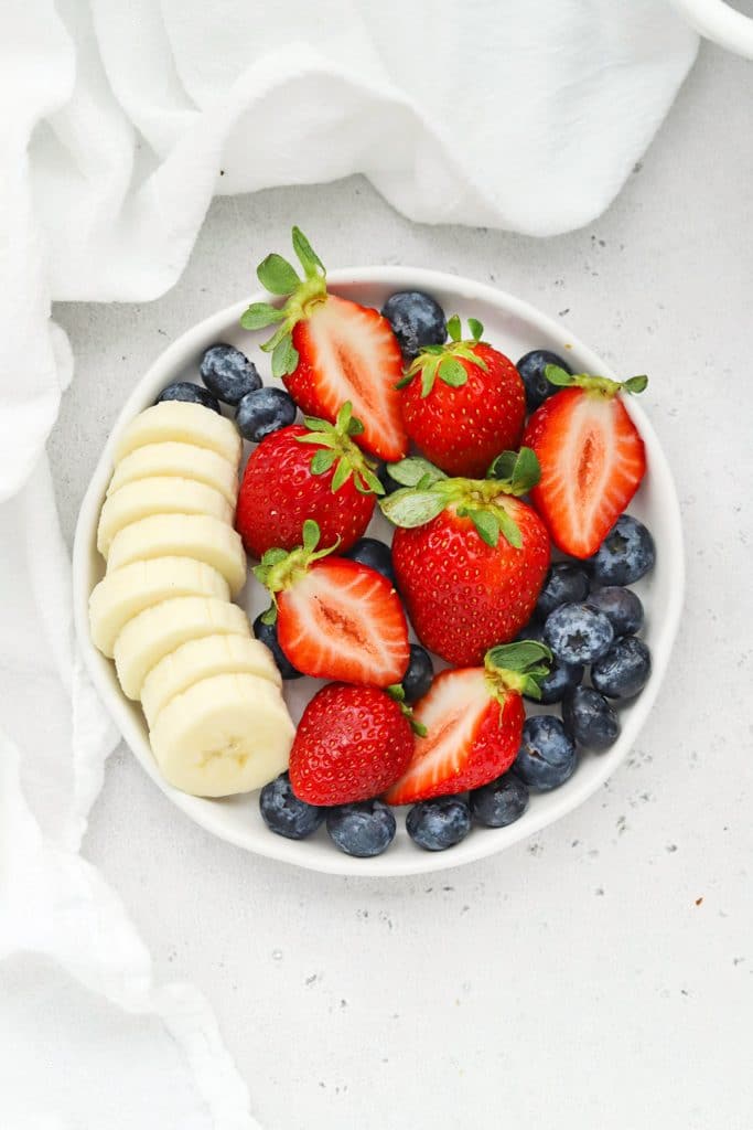 overhead view of a plate of fresh strawberries, blueberries, and sliced bananas