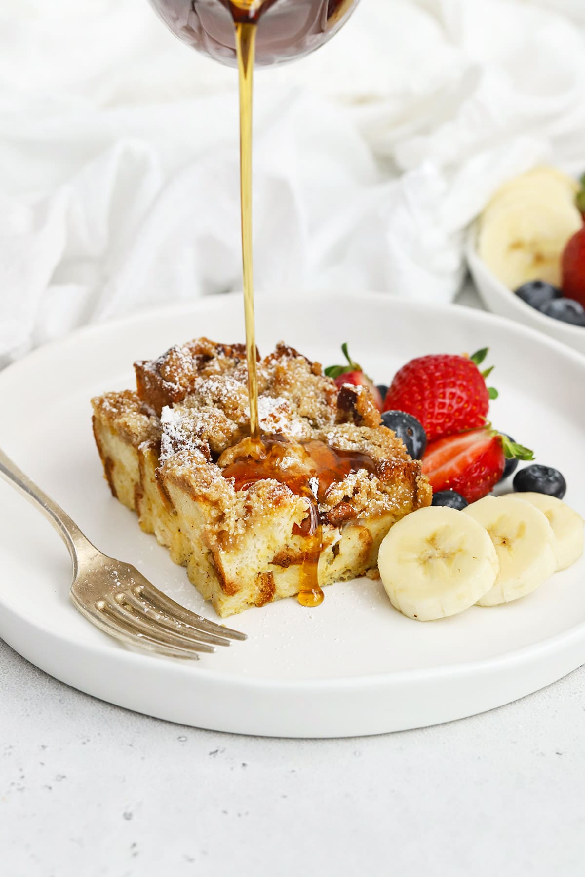 pouring maple syrup on a slice of gluten-free eggnog french toast casserole