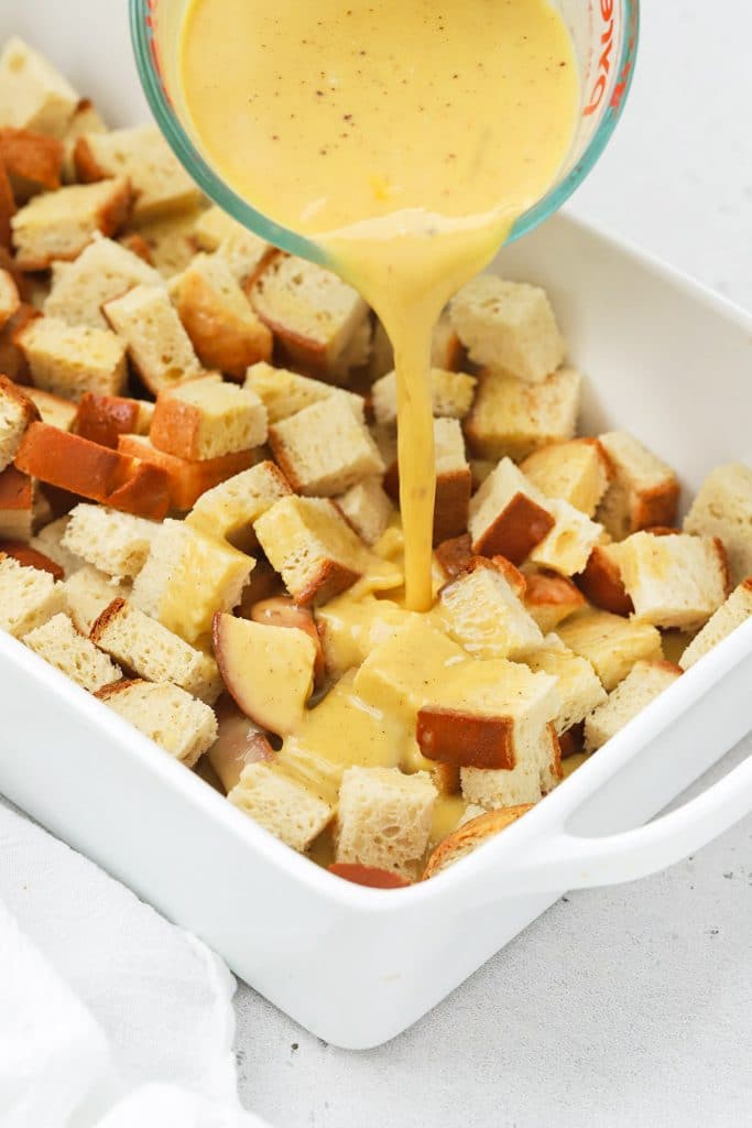 Pouring eggnog custard onto bread cubes for gluten-free eggnog french toast casserole