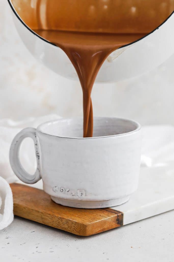 Front view of pouring creamy vegan peppermint hot chocolate into a mug