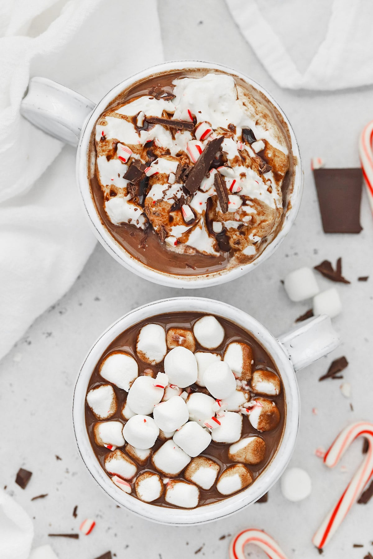 Overhead view of two mugs of vegan peppermint hot chocolate--one is topped with marshmallows, and the other is topped with coconut whipped cream