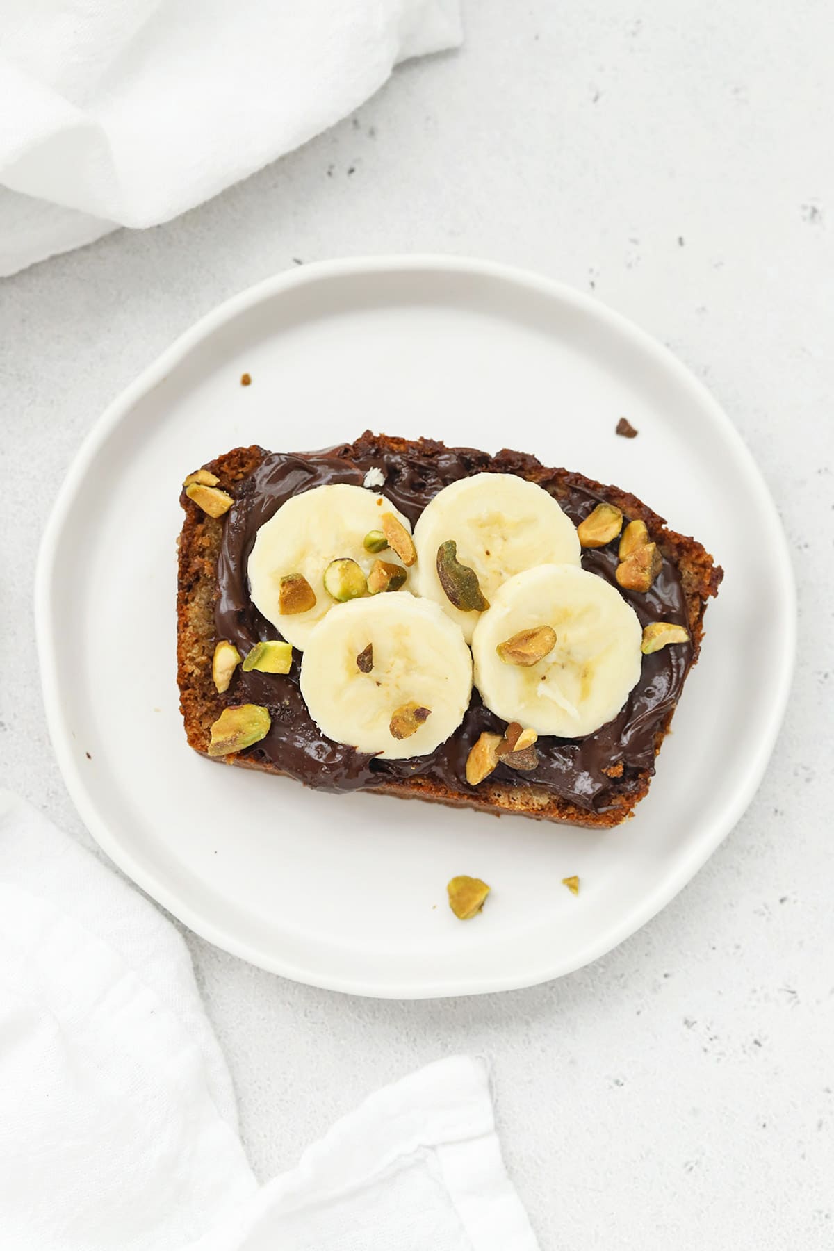 Slice of gluten-free banana bread topped with nutella, sliced bananas, and pistachios