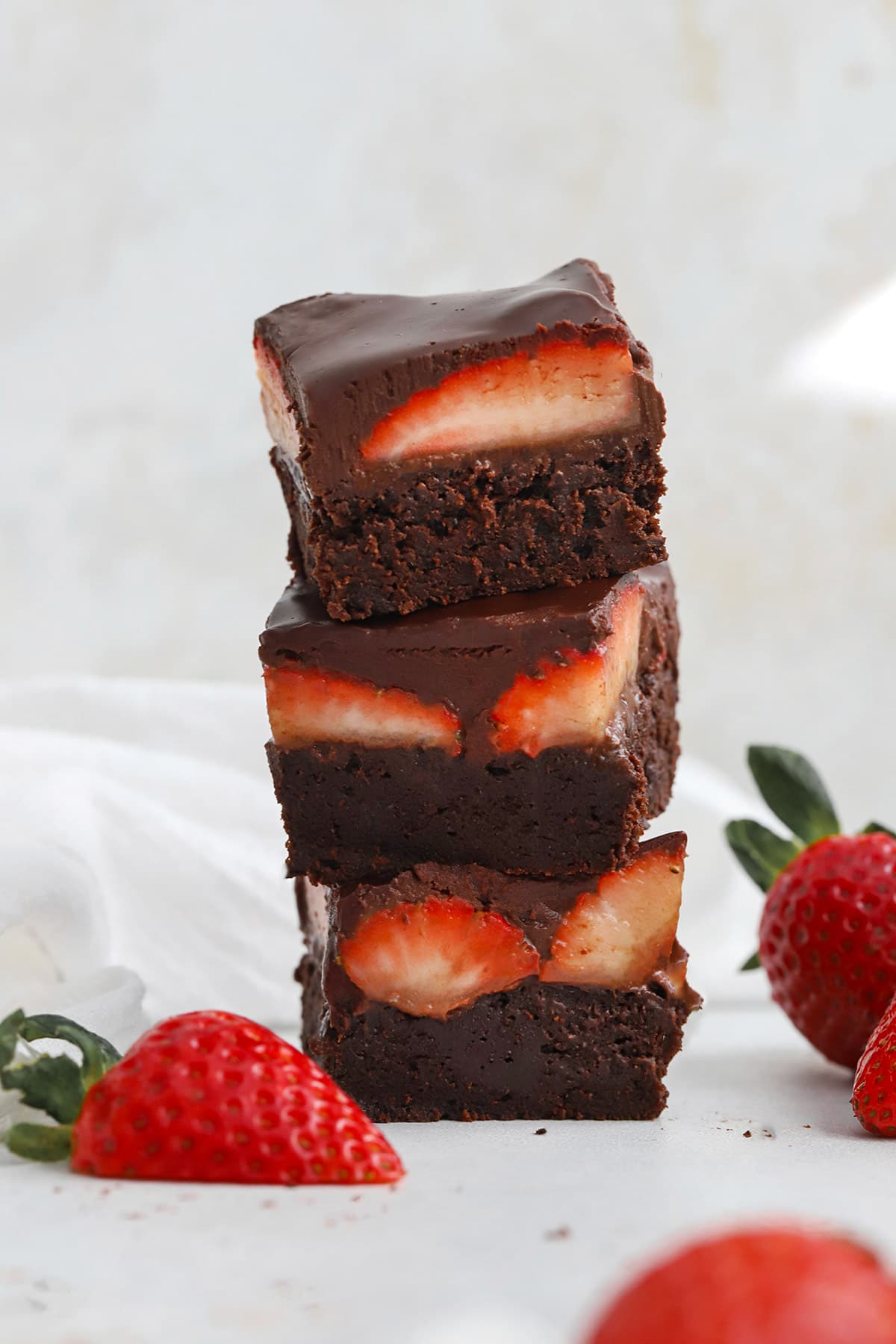 Front view of a stack of gluten-free strawberry brownies with fresh strawberries and chocolate ganache