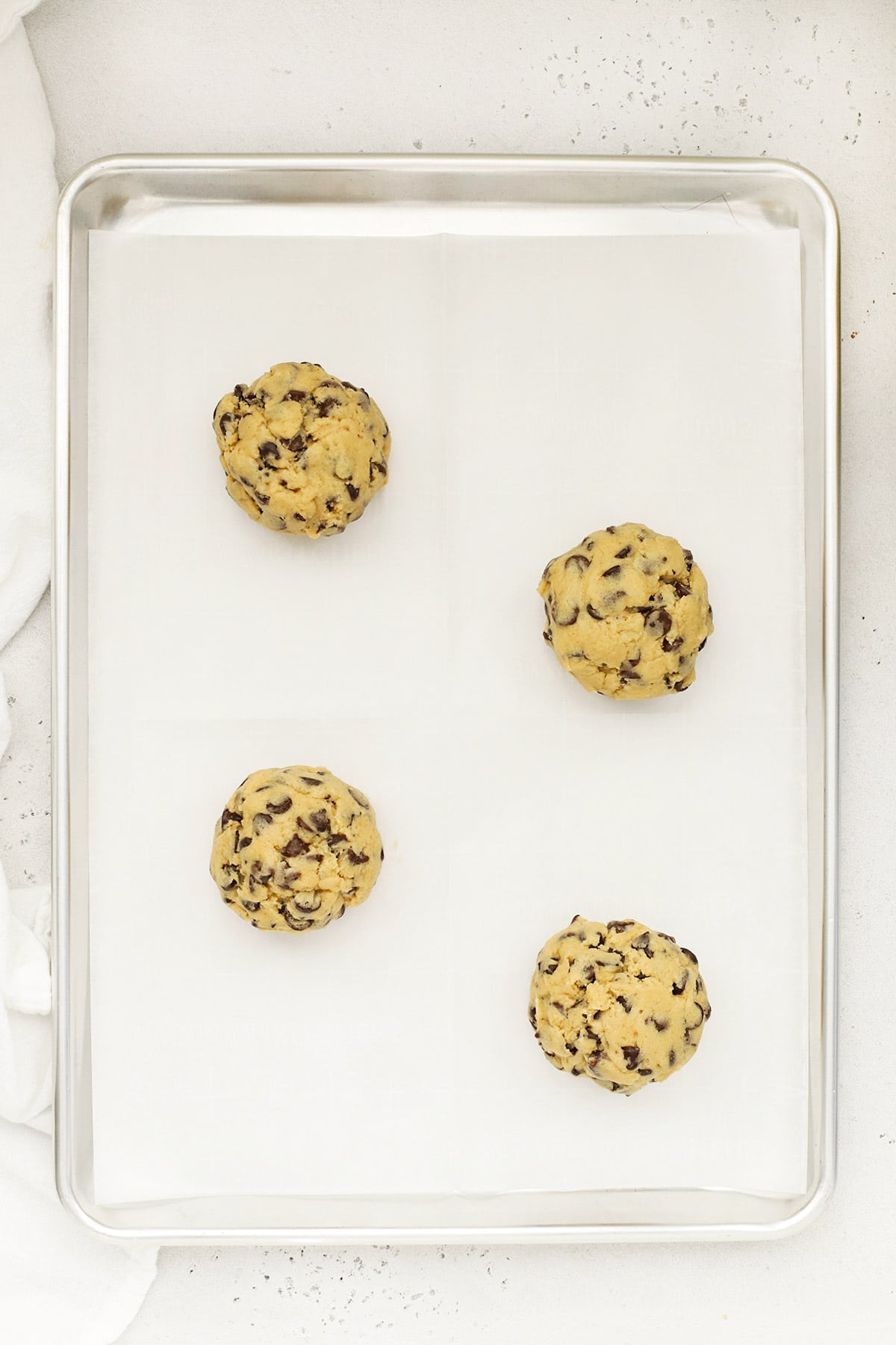 Four large balls of gluten-free Levain chocolate chip cookie dough on a baking sheet, ready to go into the oven