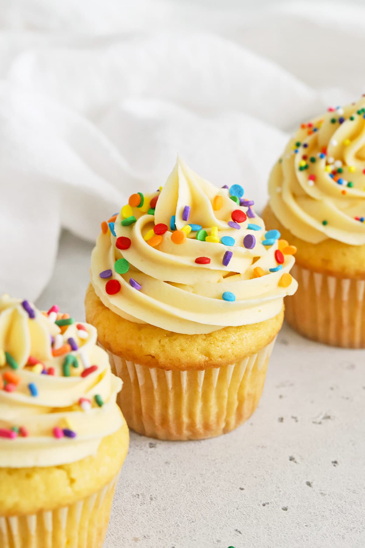 Front view of gluten-free vanilla cupcakes topped with vanilla buttercream and different kinds of sprinkles