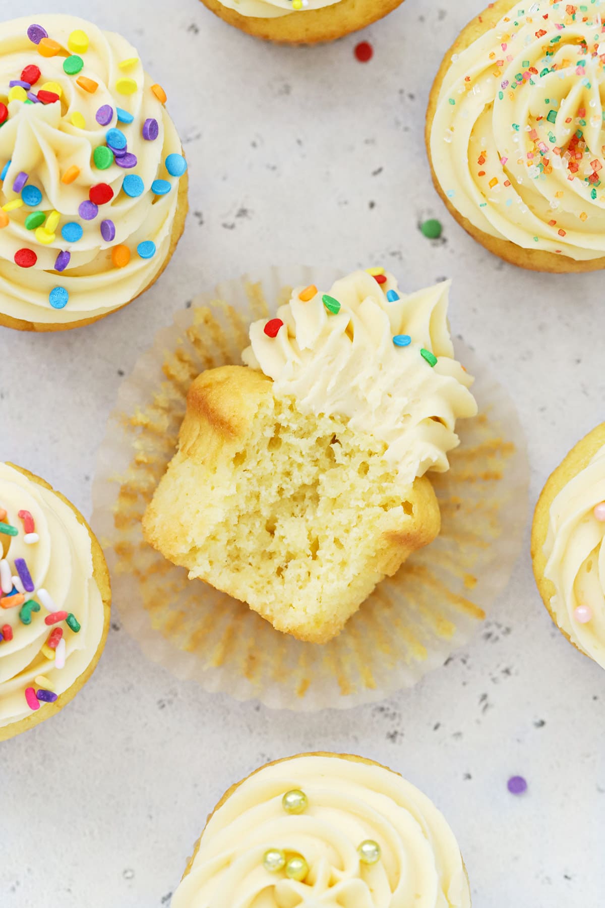 Overhead view of gluten-free vanilla cupcakes topped with vanilla buttercream and different kinds of sprinkles