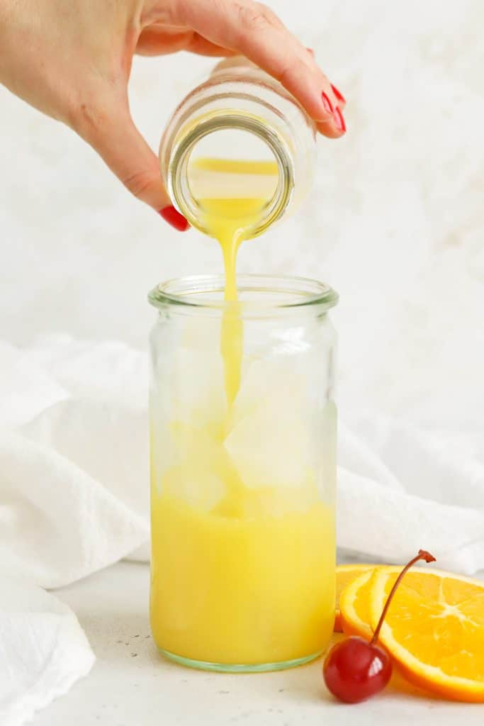 Pouring orange juice over ice to make an orange grenadine mocktail