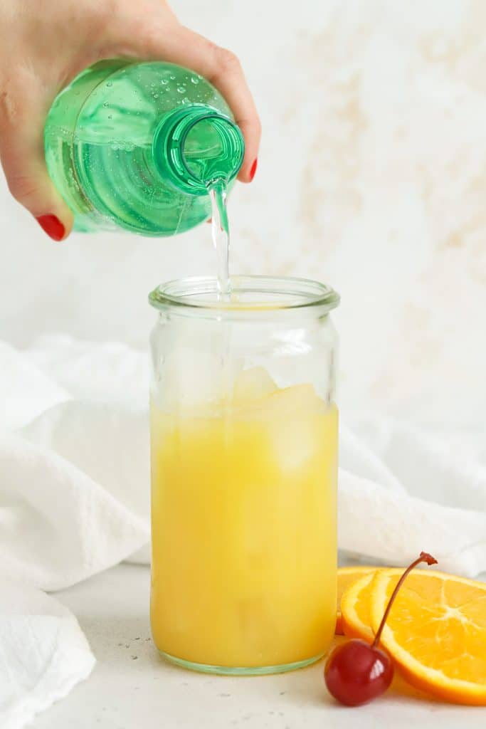 Pouring lemon lime soda over orange juice to make a virgin sunrise mocktail