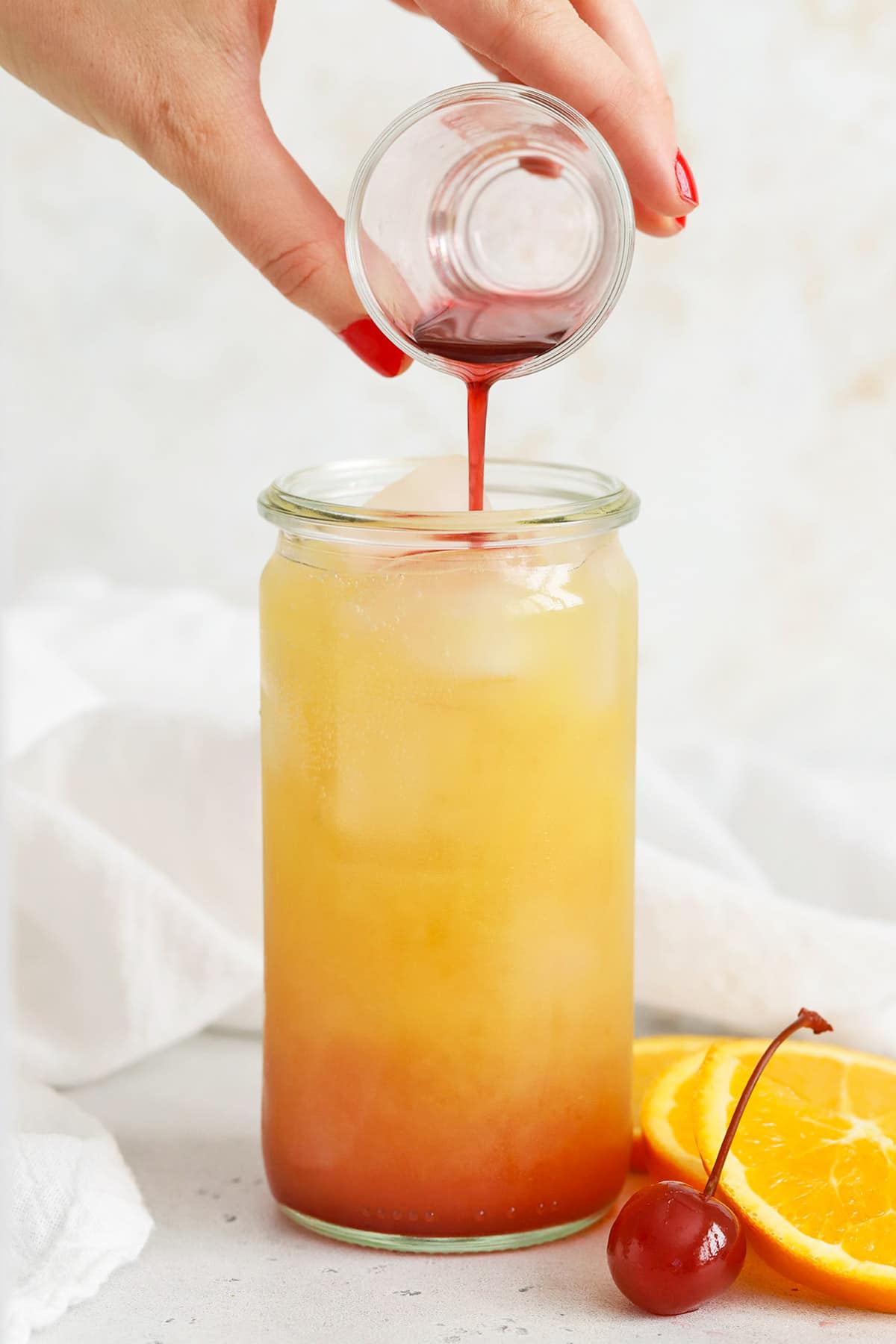 Pouring grenadine over orange juice to make a sweet sunrise mocktail