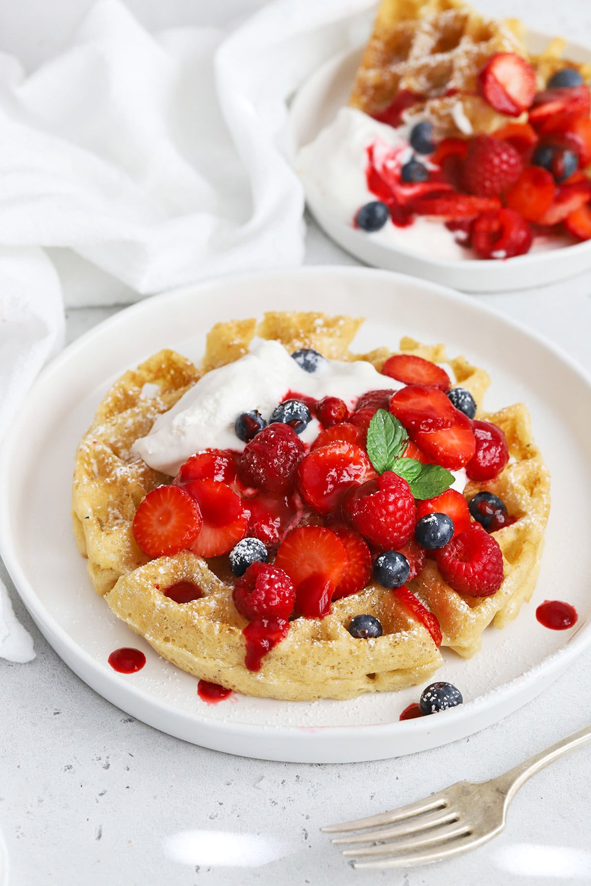 Front view of gluten-free Belgian waffles topped with berries, whipped cream, and raspberry syrup