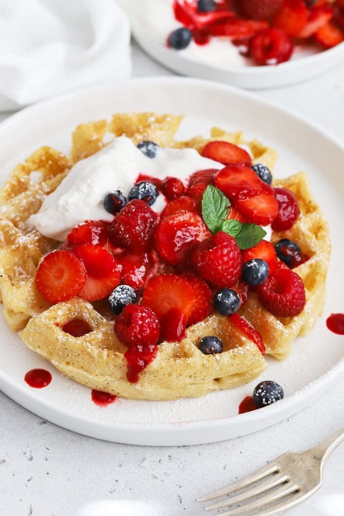 Front view of gluten-free Belgian waffles topped with berries, whipped cream, and raspberry syrup