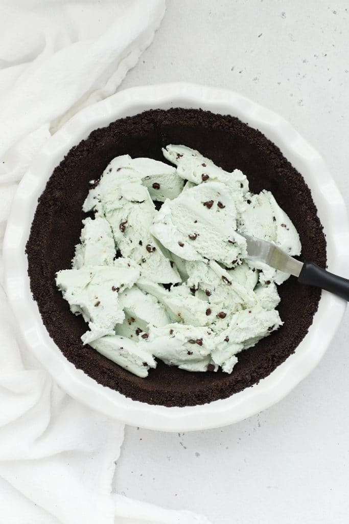 Spreading mint chocolate chip ice cream out on gluten-free oreo crust for gluten-free grasshopper ice cream pie