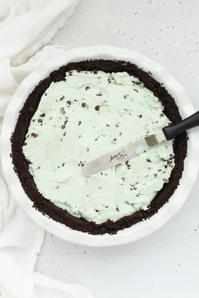 Spreading mint chocolate chip ice cream out on gluten-free oreo crust for gluten-free grasshopper pie
