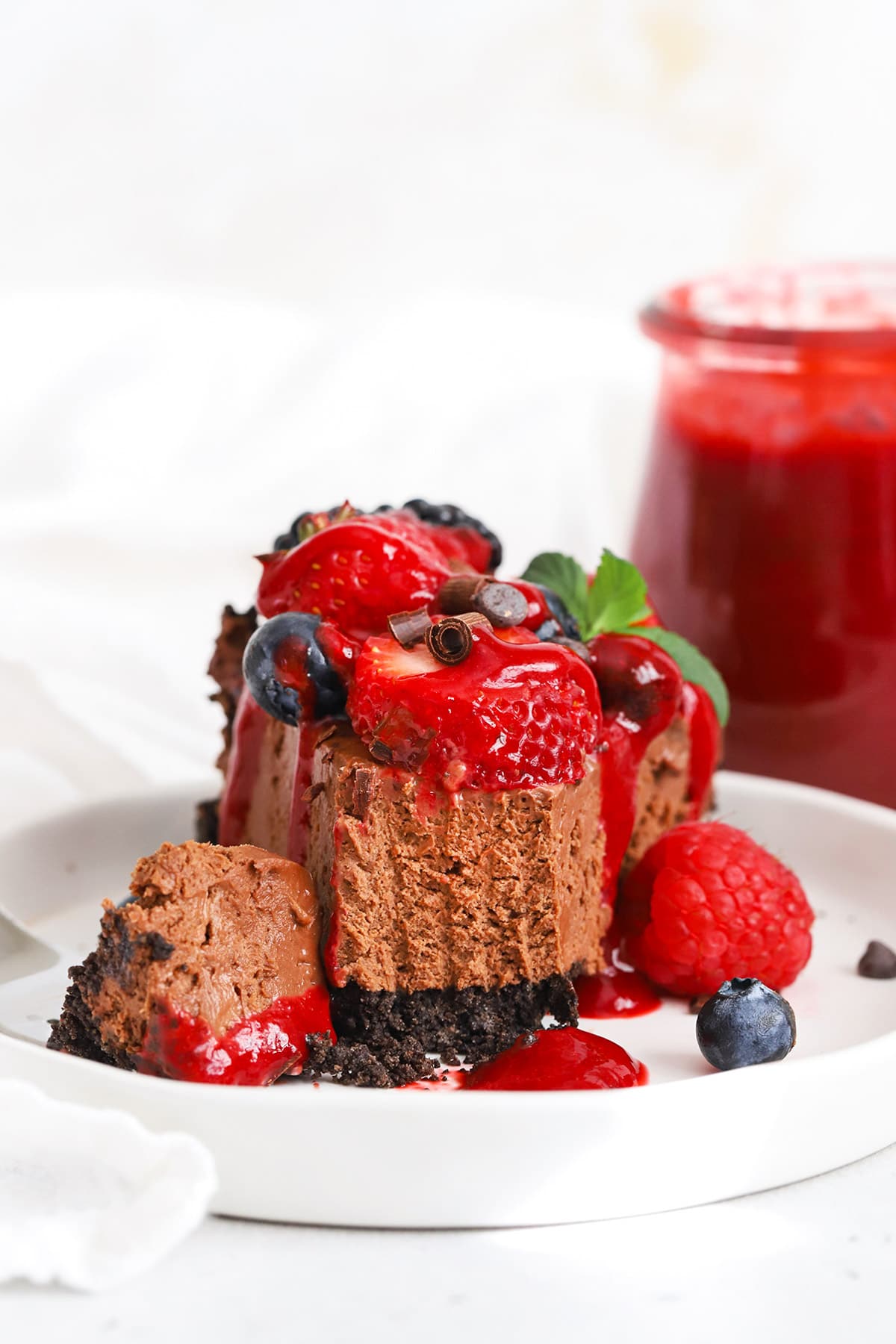 Front view of a slice of no-bake gluten-free chocolate cheesecake pie with fresh berries and raspberry sauce
