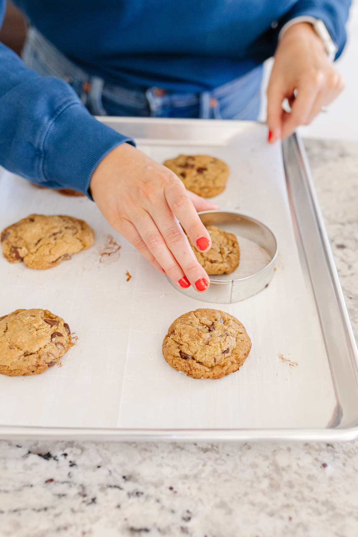 Using a large circular cookie cutter to shape freshly baked cookies into circles