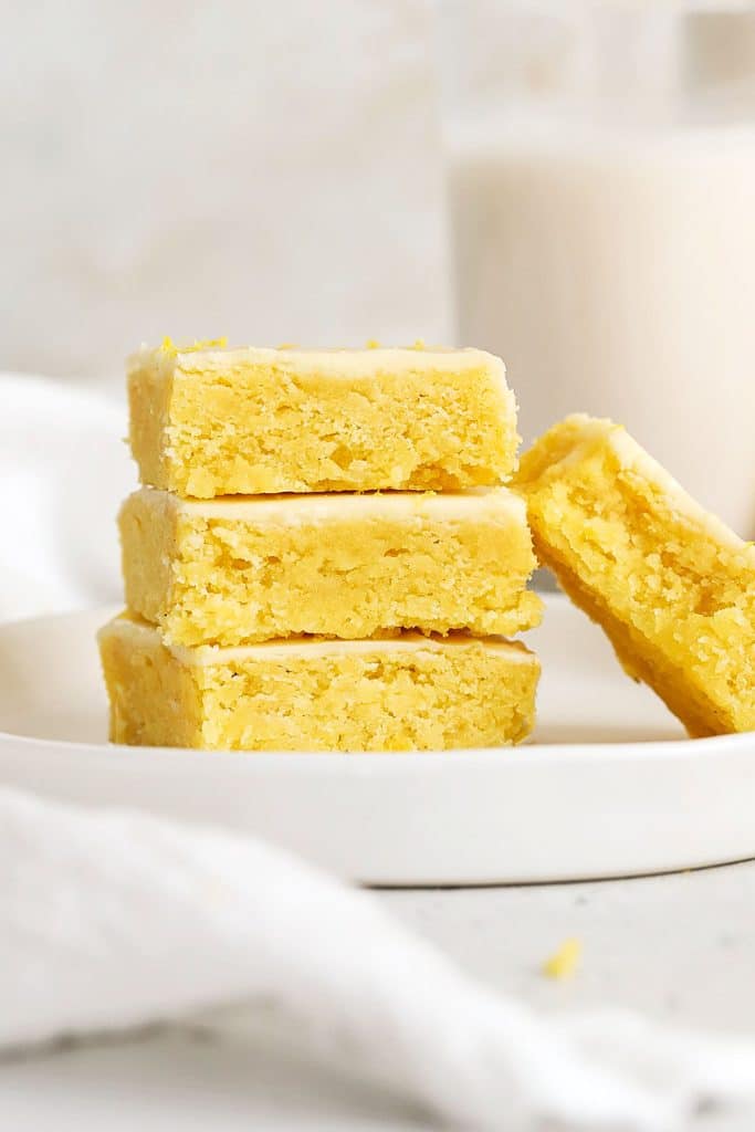 frosted gluten-free lemon brownies stacked on a white plate