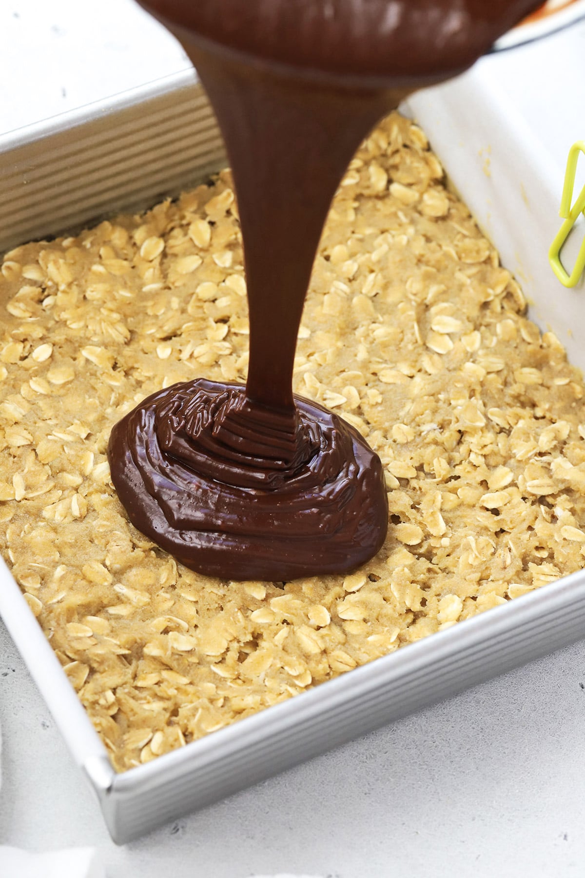 Pouring fudge filling onto an oatmeal cookie base for gluten-free oatmeal fudge bars