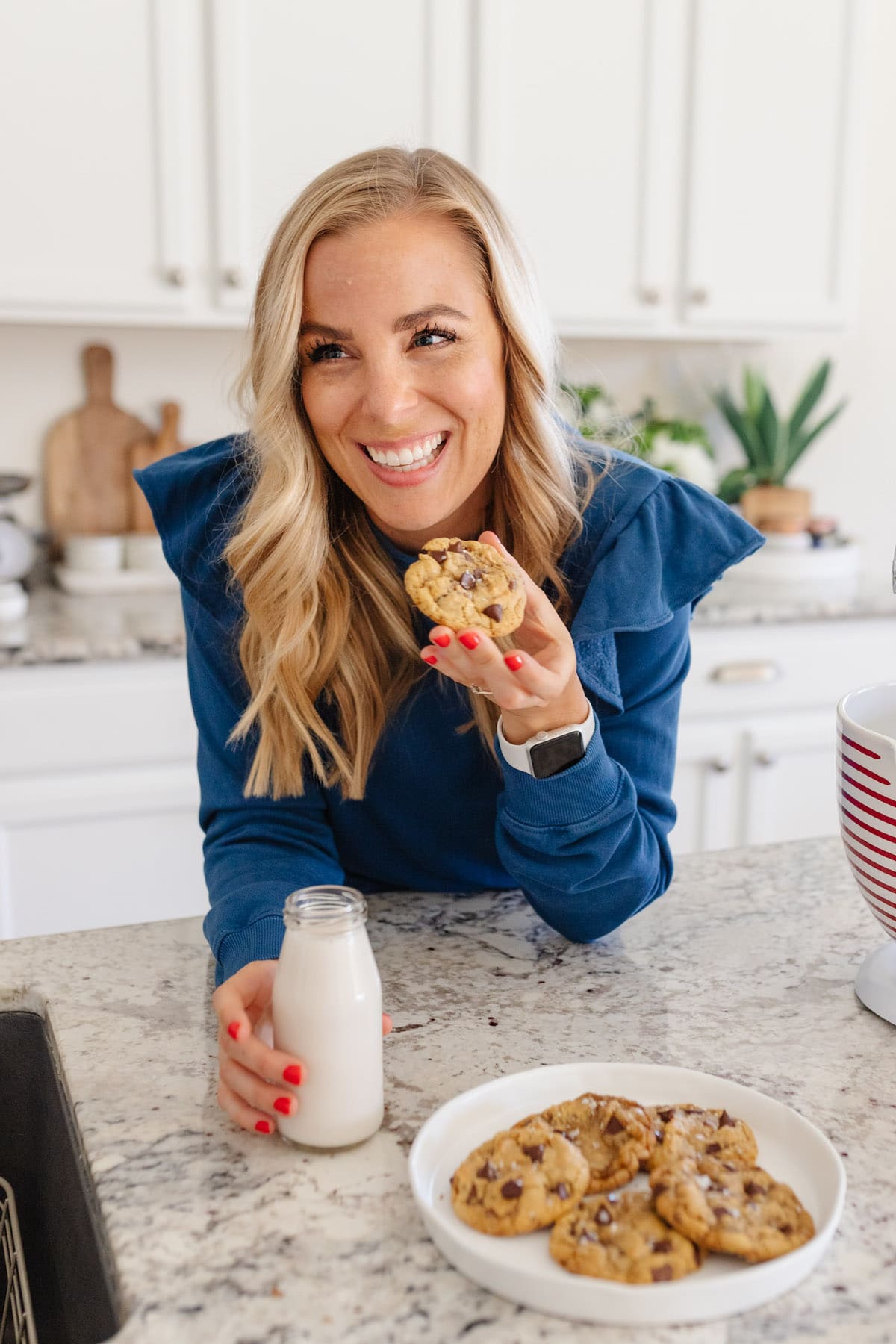 Emily Dixon from Sweets And Thank You in her kitchen eating a gluten-free cookie with almond milk