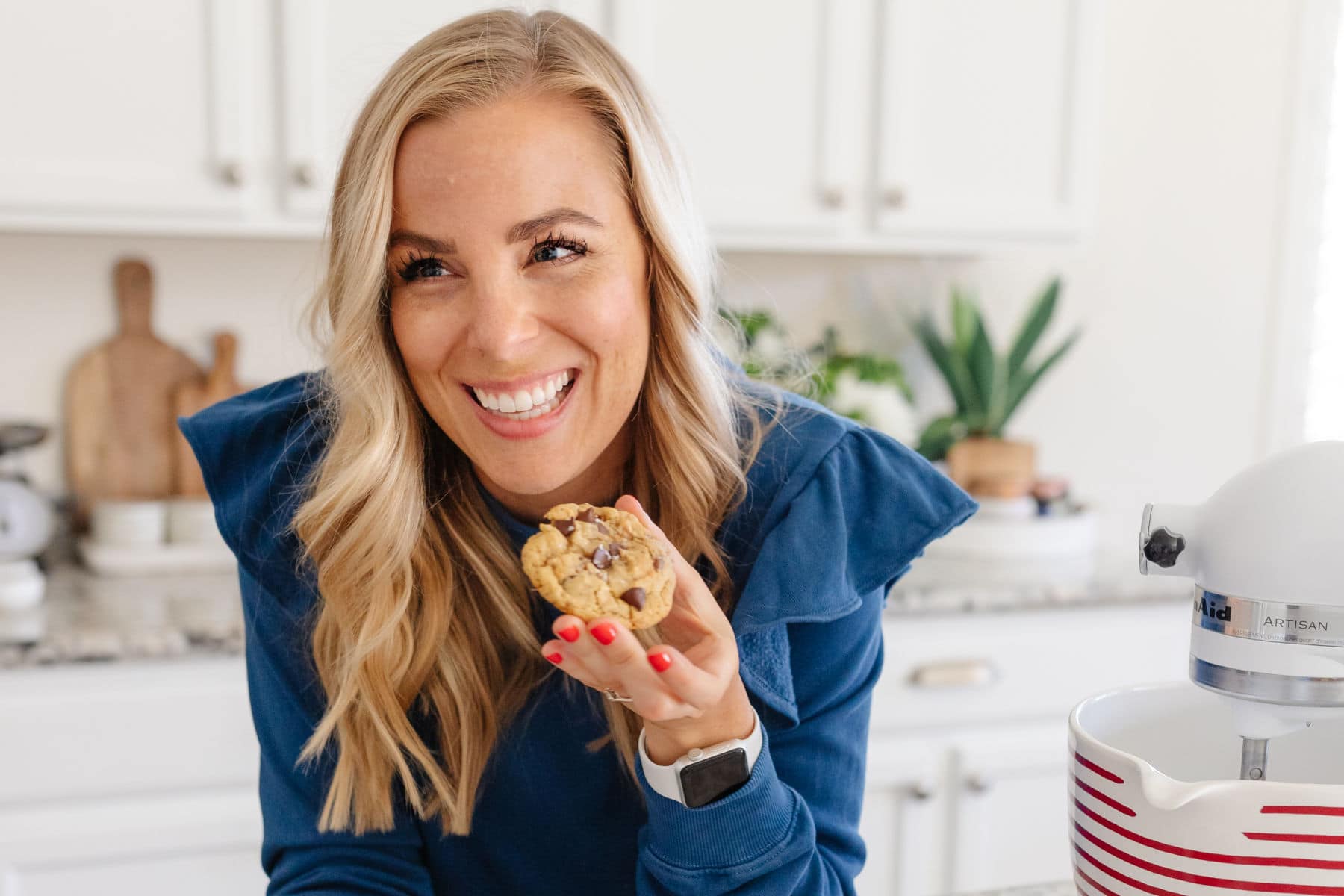 Emily Dixon from Sweets & Thank You in her kitchen eating a gluten-free cookie with almond milk