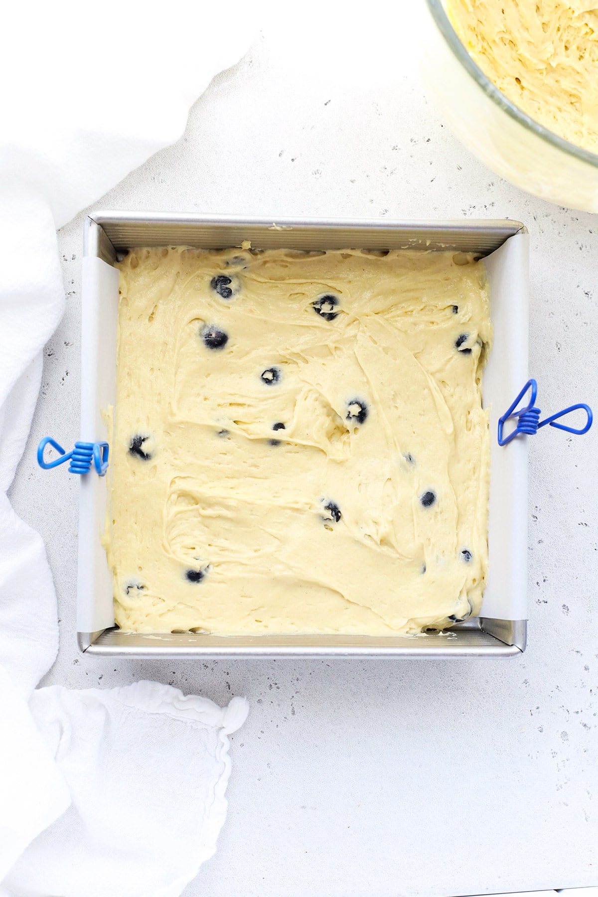 Adding gluten-free blueberry coffee cake batter to a pan