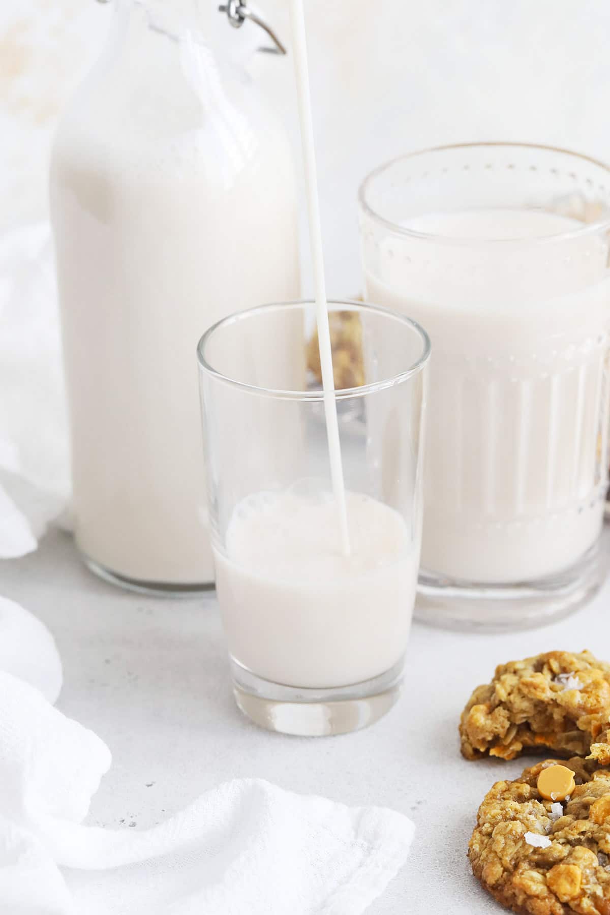 Pouring almond milk into a glass to go with gluten free oatmeal cookies