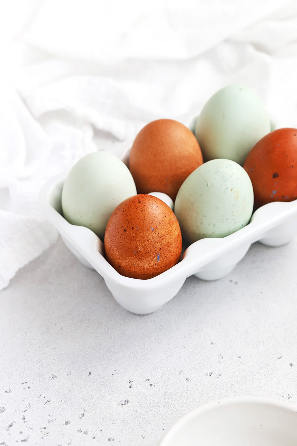 front view of muticolor farm eggs in a white egg carton