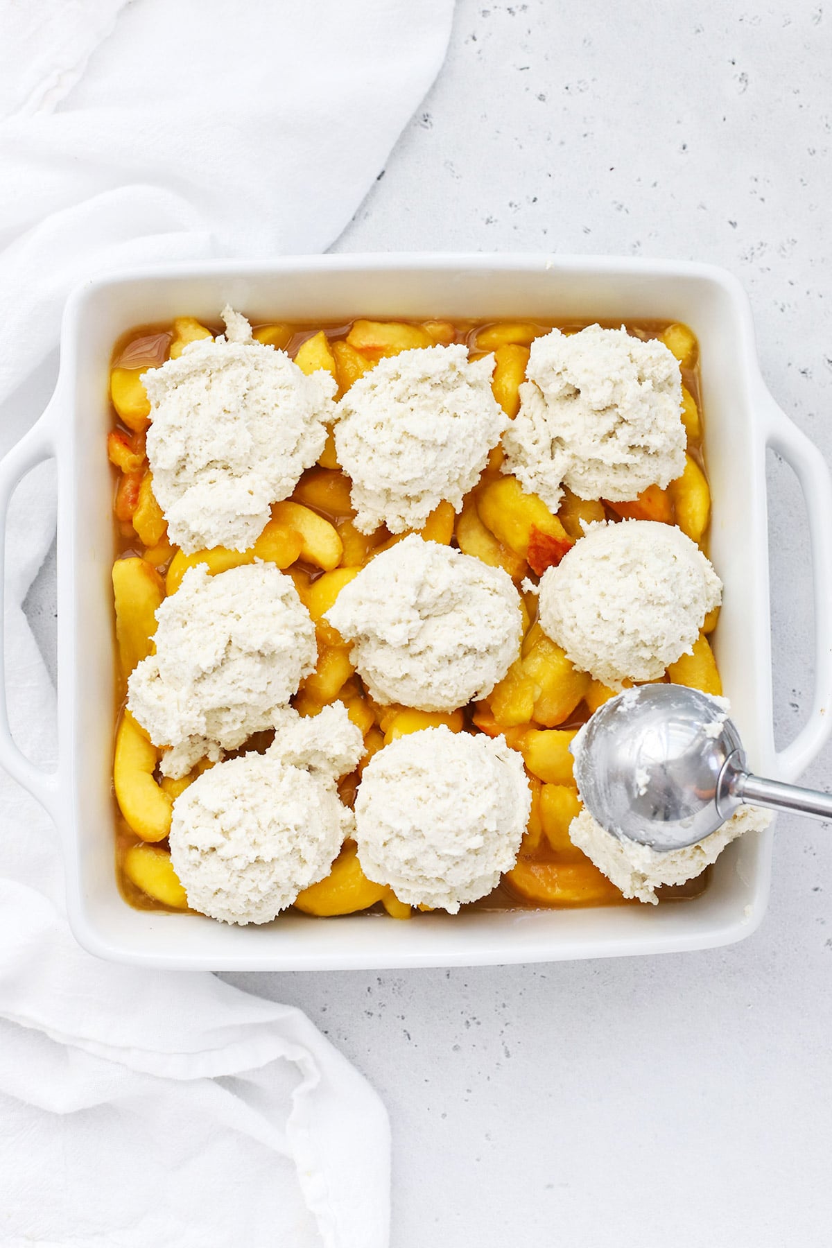 Scooping sweet gluten-free biscuit dough over the peach filling
