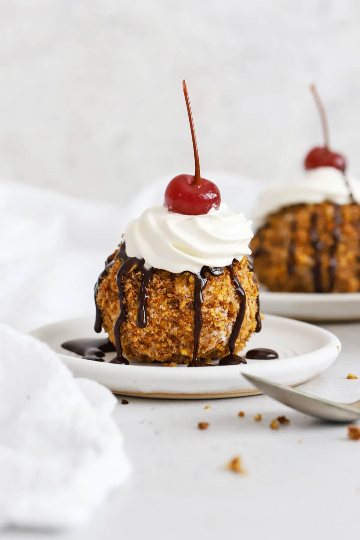 Front view of gluten-free fried ice cream topped with whipped cream, chocolate syrup, and a maraschino cherry