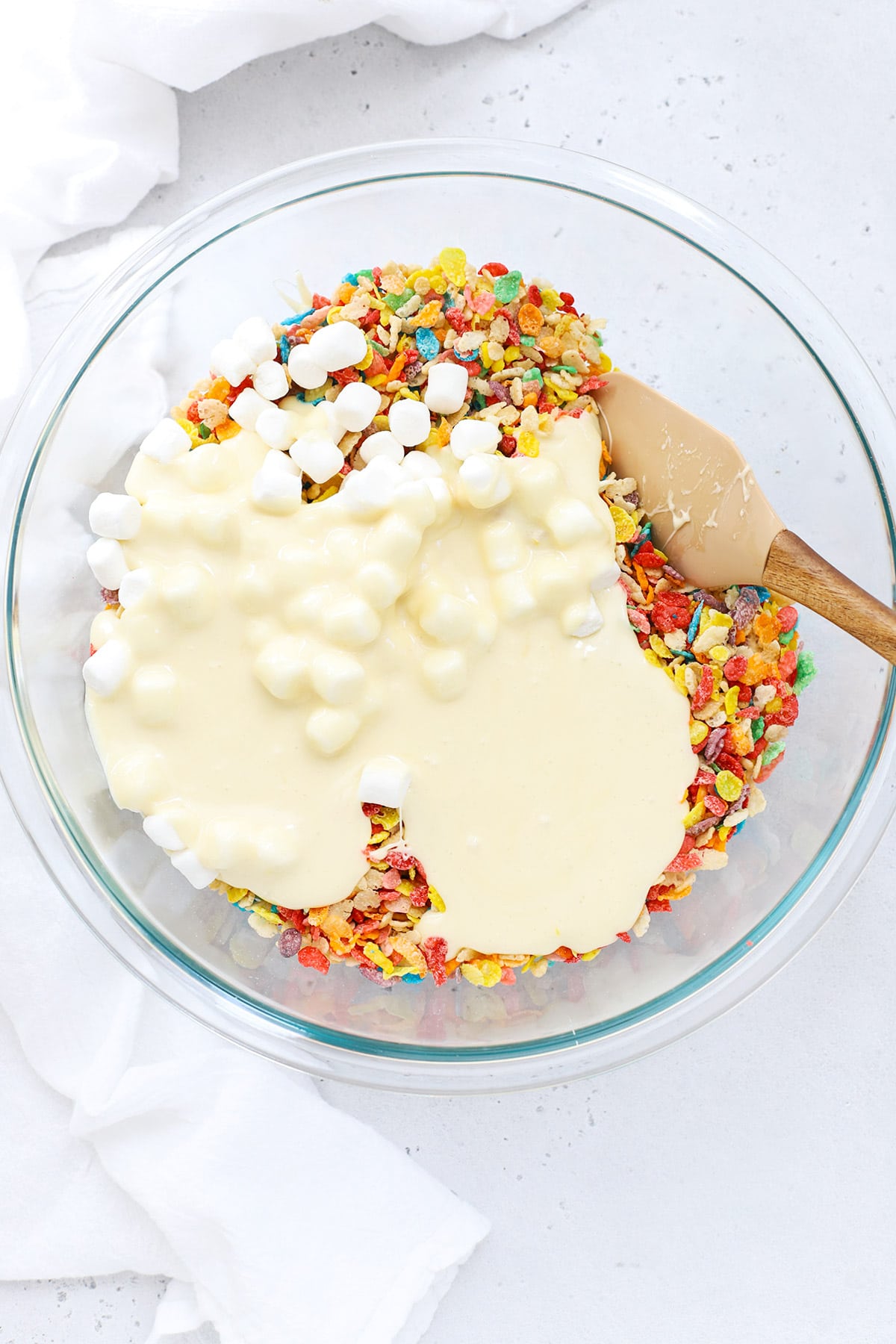adding melted marshmallow to fruity pebbles to make fruity pebbles crispy treats